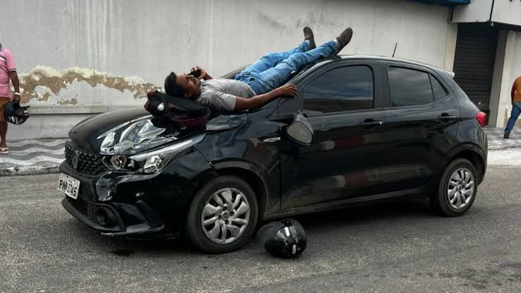 Motociclista cai sobre capô de carro após acidente e usa celular enquanto aguarda socorro