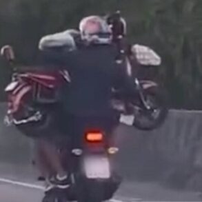 Homem pilota moto enquanto garupa carrega outro veículo